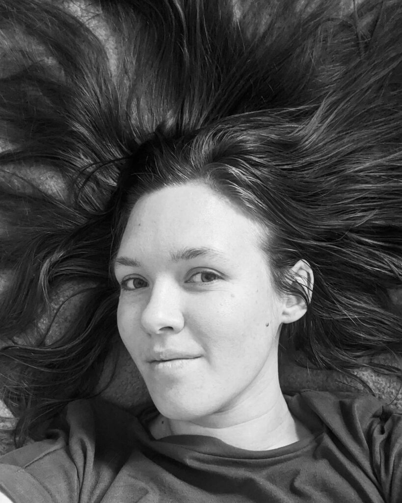 An up-close black and white photo of Kate looking at the camera and smiling with her hair splayed out all around her.